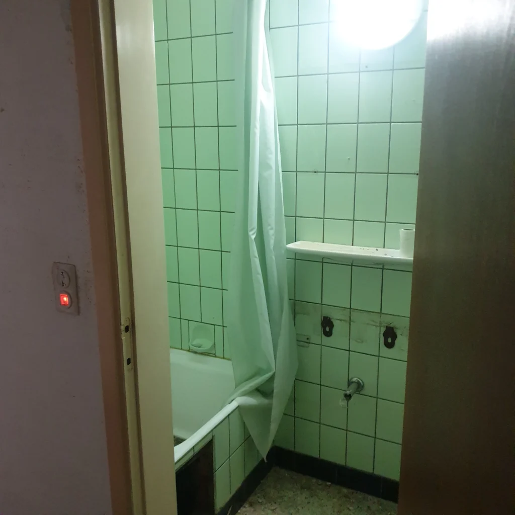 Stara strefa prysznicowa wykończona zielonymi płytkami przed remontem.